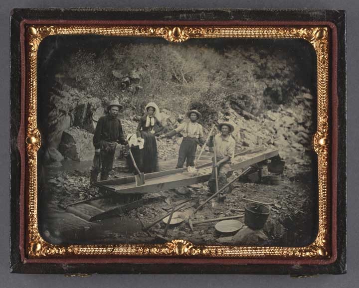 This dagguerreotye shows a woman and three men standing around a long-tom situated in a streambed.